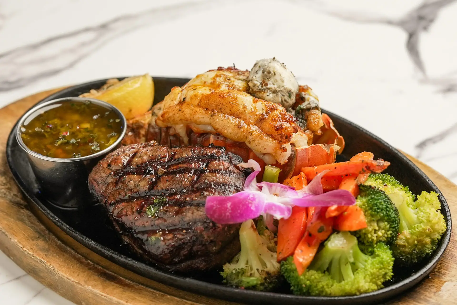 SURF AND TURF Grilled filet mignon w /Lobster tail, served in cast iron skillet flam be, mixed vegetables, topped w /honey herb butter