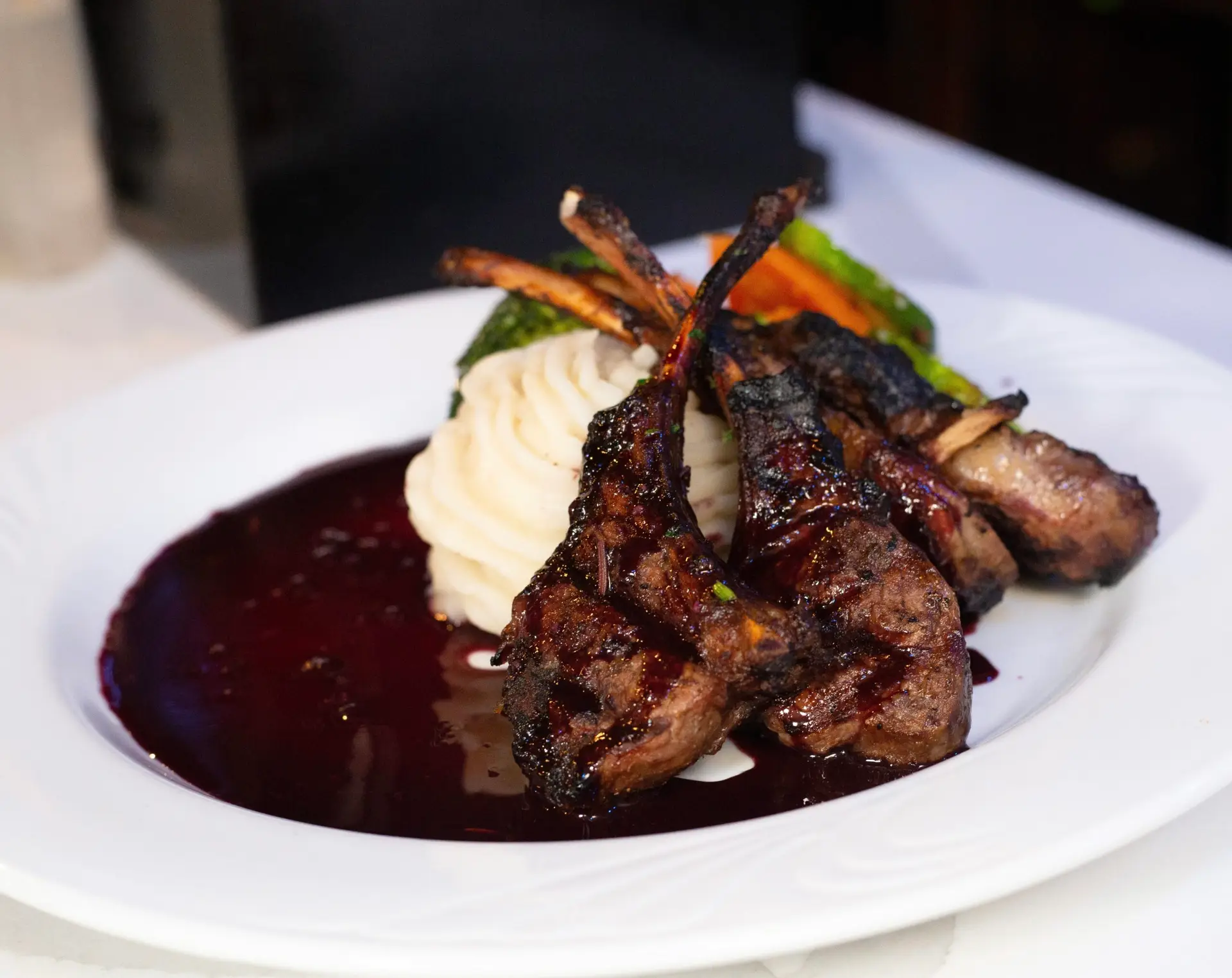 LAMB CHOPS served with mashed potatoes, broccoli, carrots, and red wine reduction sauce.